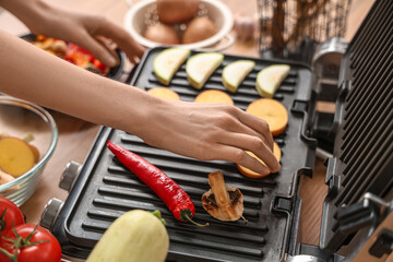 Wall Mural - Young woman cooking tasty vegetables on modern electric grill in kitchen