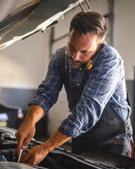 Car mechanic work on a car engine with a wrench and talk on cellphone