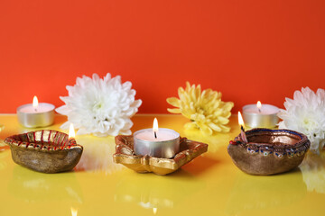 Diya lamps with beautiful flowers and burning candles on color background. Divaly celebration