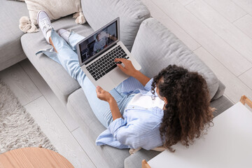 Sticker - Pretty young African-American woman with laptop lying on sofa at home