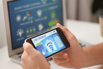 Canvas Print - Young man using mobile phone with smart home application in room, closeup