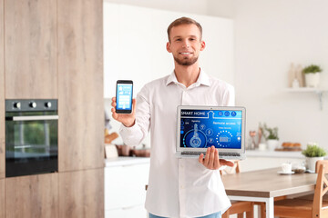 Canvas Print - Young man holding mobile phone and laptop with smart home application in kitchen