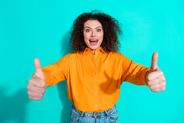 Wall Mural - Photo of ecstatic woman with wavy hairstyle dressed orange t-shirt showing you thumb up good job isolated on turquoise color background