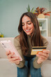 © Jose Calsina - Vertical Young woman using a smart phone to make an online purchase with a credit card sitting at home sofa. Female looking for a delivery with a cellphone at living room couch. Girl shopping online