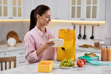 Wall Mural - Woman with bag packing school lunch box and healthy food at white marble table in kitchen