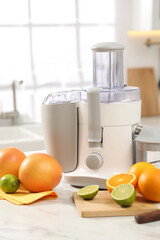 Modern juicer, oranges and limes on white marble table in kitchen