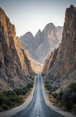 A straight highway leading through a mountain pass, with towering peaks on either side and a clear sky above