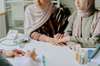 © AnnaStills - Two women wearing hijabs are discussing medical treatment with a doctor while sitting at hospital table holding hands showing support and concern