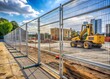 © Curie - 'Temporary fencing with durable steel mesh and hinges, enclosing a large construction site with heavy machinery and building materials'