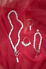 Wall Mural - Glass white beaded necklace and earrings set on the red fabric background