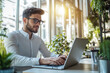 © kitipol - High-resolution brightly lit photorealistic candid photograph of a young professional marketer typing on his laptop in a stylish office with natural light. The photograph is styled like a high-end