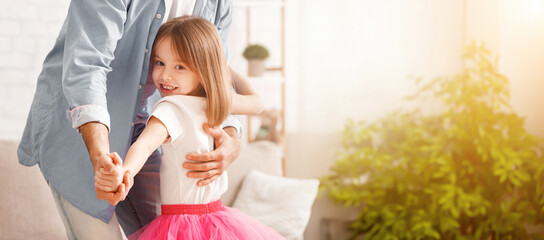 Cropped of dad teaching little daughter dancing at home, girl staying on father feet and smiling at camera