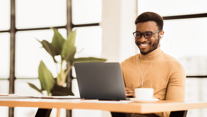 Happy African Student Studying With Laptop In University Cafe Wearing Headphones. Panorama, copy space