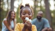 © Coosh448 - Black little girl eating roasted marshmallows while camping with parents in woods.