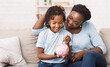 © Prostock-studio - African Mother And Daughter Putting Coins Into Piggy Bank At Home. Free space