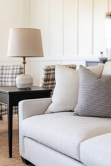 Wall Mural - A close-up shot of the sofa in the foreground, featuring soft white linen fabric and plush gray cushions. The background is a minimalist living room with light wood flooring, a black side table.