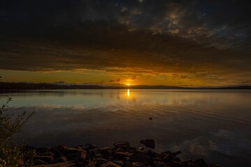 Wall Mural - Sunset over a calm lake with a rocky shoreline.