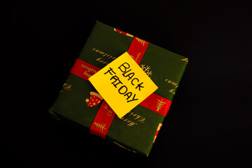 Green Christmas gift with a message on a yellow paper that says Black Friday on a black background, Christmas shopping concept discounts related to Black Friday