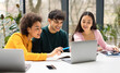 © Prostock-studio - Happy international students friends sitting at desk in coworking space and using laptop, making project together or watching educational video, panorama