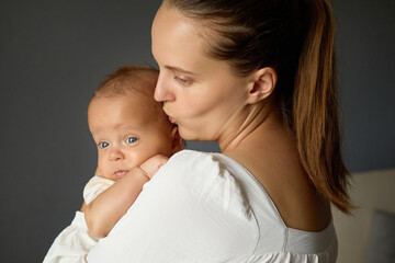 Caucasian woman kissing lovingly her cute little infant expressing joy and care during beautiful moment of motherhood at home mother and baby together in loving embrace