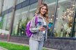© deagreez - Portrait of pretty young girl use phone drink coffee backpack wear denim jacket walk street outdoors