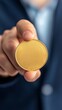 © sorrakrit - Close up of a hand holding out a gold coin.  The coin is shiny and new.  The person is wearing a suit jacket.