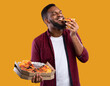 © Prostock-studio - Happy African Young Man Enjoying Pizza Biting Tasty Slice Posing With Box Over Yellow Background. Junk Food Lover Eating Italian Pizza In Studio. Unhealthy Male Nutrition And Cheat Meal