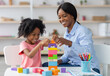 © Prostock-studio - Adorable black kid curly little girl and child development specialist attractive young woman playing with colorful wooden bricks, sitting at table and making pyramid together, smiling