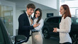 © Yuliia - Caucasian couple buyers clients talking with woman dealer saleswoman salon showroom rental service transport rent manager consulting help choosing buying luxury modern car talk showing automobile sale