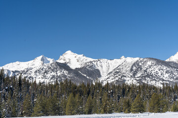 A sunny view of the Teton Mountain Range covered in snow during a cold winter.