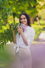 Wall Mural - Vertical hoto of pretty young good mood girl posing smell lilac flowers bush wear white clothes walk outside urban city park