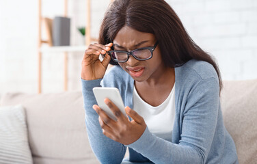 Can not believe my eyes. Sceptical afro woman in eyeglasses reading unexpected message on smartphone, full of disbelieve or having vision problem