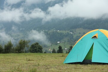 Wall Mural - Camping tent on green grass in mountains, space for text