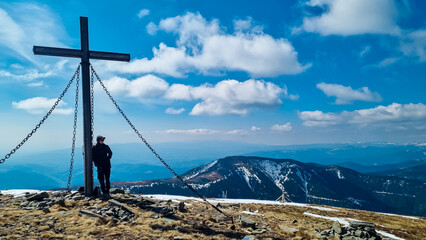 Wall Mural - Hiker man reaching wooden summit cross standing atop mountain peak Lenzmoarkogel, Gleinalpe, Lavanttal Alps, Styria, Austria. Hiking trail on snow covered alpine meadow. Wanderlust. Tranquil serene