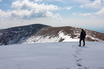 Wall Mural - Hiker man on scenic hiking trail over snow covered alpine meadows and rolling hills to snow-capped mountain peak Lenzmoarkogel, Gleinalpe, Lavantal Alps, Styria, Austria. Wanderlust in Austrian Alps