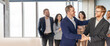 © Prostock-studio - Two professionals shake hands, marking a successful agreement in a contemporary office. Colleagues stand nearby, expressing joy and excitement for the achievement.