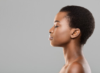 Wall Mural - Natural beauty concept. Side view portrait of young beautiful afro woman with flawless skin standing with closed eyes over gray background, copy space