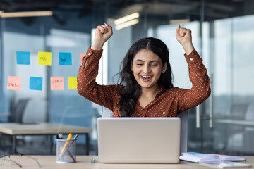 Successful business woman celebrates triumph and victory, woman at workplace received a positive result of achievement, female worker rejoices holding hands up, victory gesture.