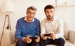 © Prostock-studio - Mature Son And Elderly Father Playing Video Game Having Fun Together Sitting On Sofa Indoor. Different Generations Friendship