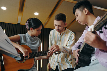music instructor teaching guitar techniques to two young students. the students are holding guitars 