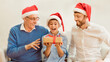 © Prostock-studio - Christmas. Father And Grandfather Giving Excited Boy Xmas Gift Sitting On Sofa At Home. Panorama, Selective Focus
