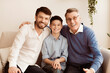 © Prostock-studio - Male Generation. Happy Grandfather With Son And Grandson Smiling At Camera Hugging Sitting Together On Couch At Home.