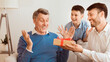 © Prostock-studio - Adult Son And Grandson Giving Grandfather Gift Congratulating Him On His Birthday Sitting On Sofa At Home. Panorama