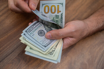 Aufkleber - Hands counting US dollar banknotes on a wooden surface. Cash handling and financial management concept. Perfect for themes of personal finance, budgeting, and economic transactions 