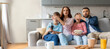 © Prostock-studio - A family of four sits on a couch in their living room, expressing surprise as they watch a thrilling movie. They hold snacks and a phone, highlighting the interactive home experience.