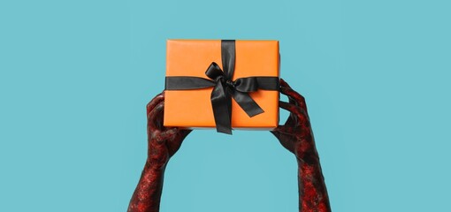 Wall Mural - Hands of zombie with gift box on blue background. Halloween celebration