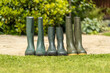 © Tosh - 3 pairs mid and full height green rubber outdoor gardening wellington boots lined up in row on garden patio circle