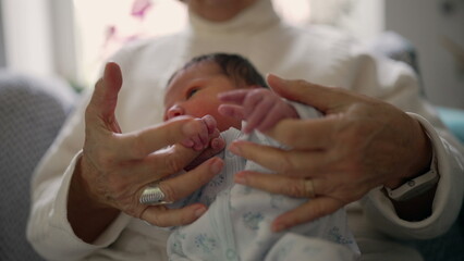 Close-up of an elderly woman's hands cradling a newborn baby dressed in a soft onesie, capturing a moment of gentle care, love, and the delicate bond between generations