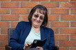 © Tosh - Woman sat in chair beside brick house on mobile phone smiling