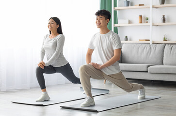 Motivated asian young couple exercising together at home, positive korean man and woman in sportswear standing on fitness mat, stretching and smiling, copy space. Healthy lifestyle concept